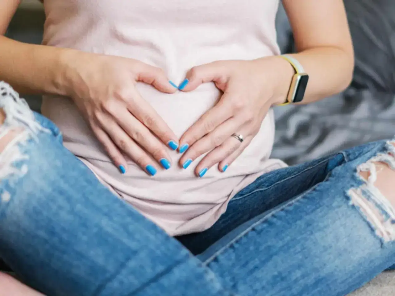 Schwangere Frau mit blauem Nagellack formt Herz auf Bauch. Ein Zeichen f&uuml;r die Vorfreude auf das Baby, auch mit Nagellack in der Schwangerschaft.