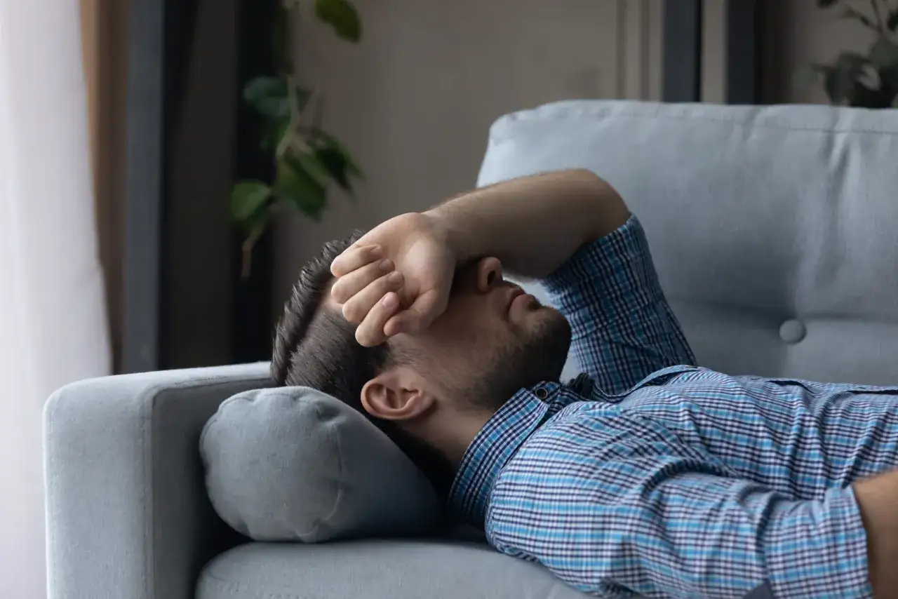 Mann liegt ersch&ouml;pft auf Sofa, Hand vor dem Gesicht. Er sucht nach Tipps, wie man nach Koks schlafen kann, um wieder zur Ruhe zu finden.