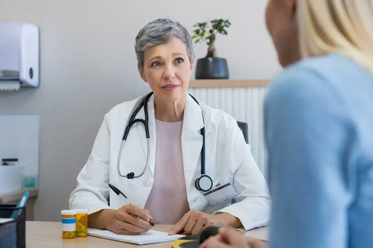 &Auml;rztin erkl&auml;rt einer Patientin, was tun gegen Schwindel. Sie sitzt am Schreibtisch mit Stethoskop und Notizblock.