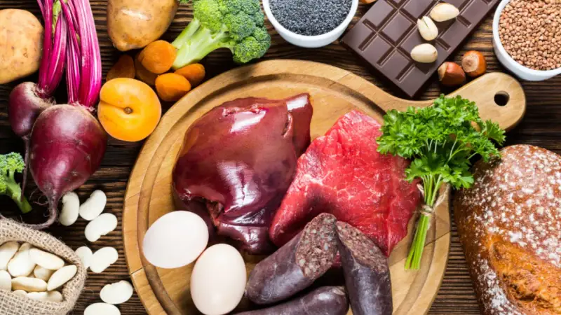 Eine Auswahl an eisenhaltigen Lebensmitteln: Rindfleisch, Leber, Blutwurst, Eier, Linsen, Rote Bete, Spinat, Brokkoli, Aprikosen, Schokolade und Vollkornbrot.